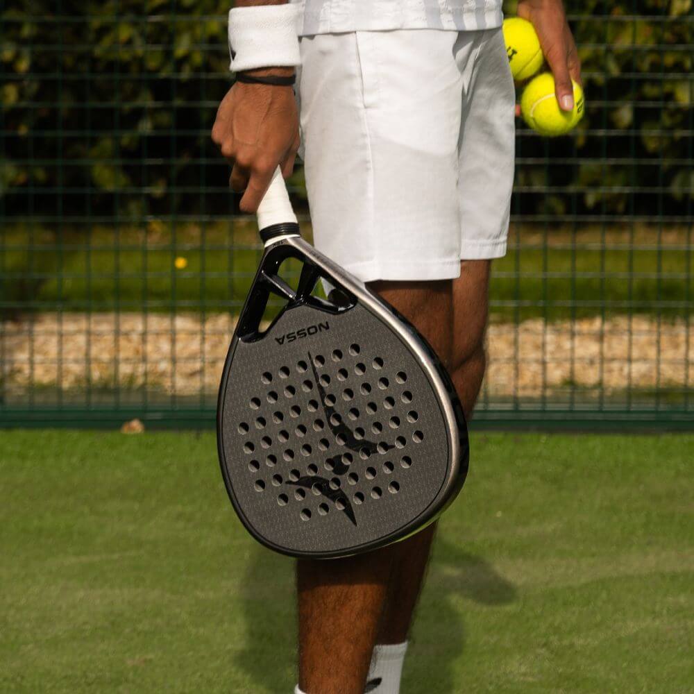 Player holding the black NOSSA Padel CORE racket and padel balls on court