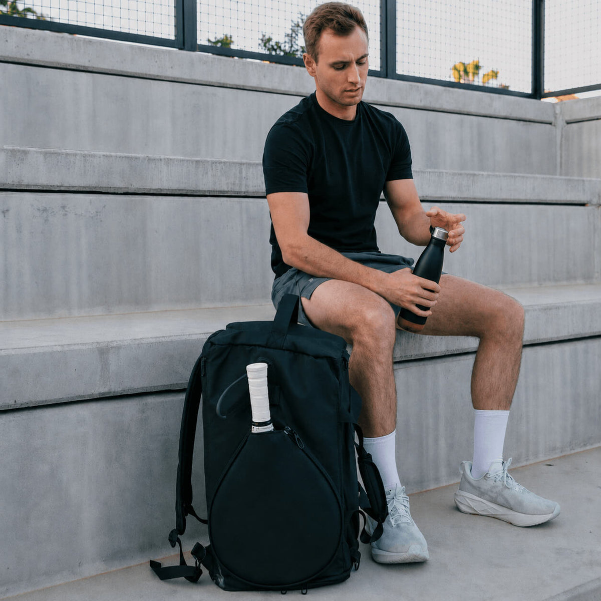 Player sitting courtside with the black NOSSA Padel HYBRID rucksack
