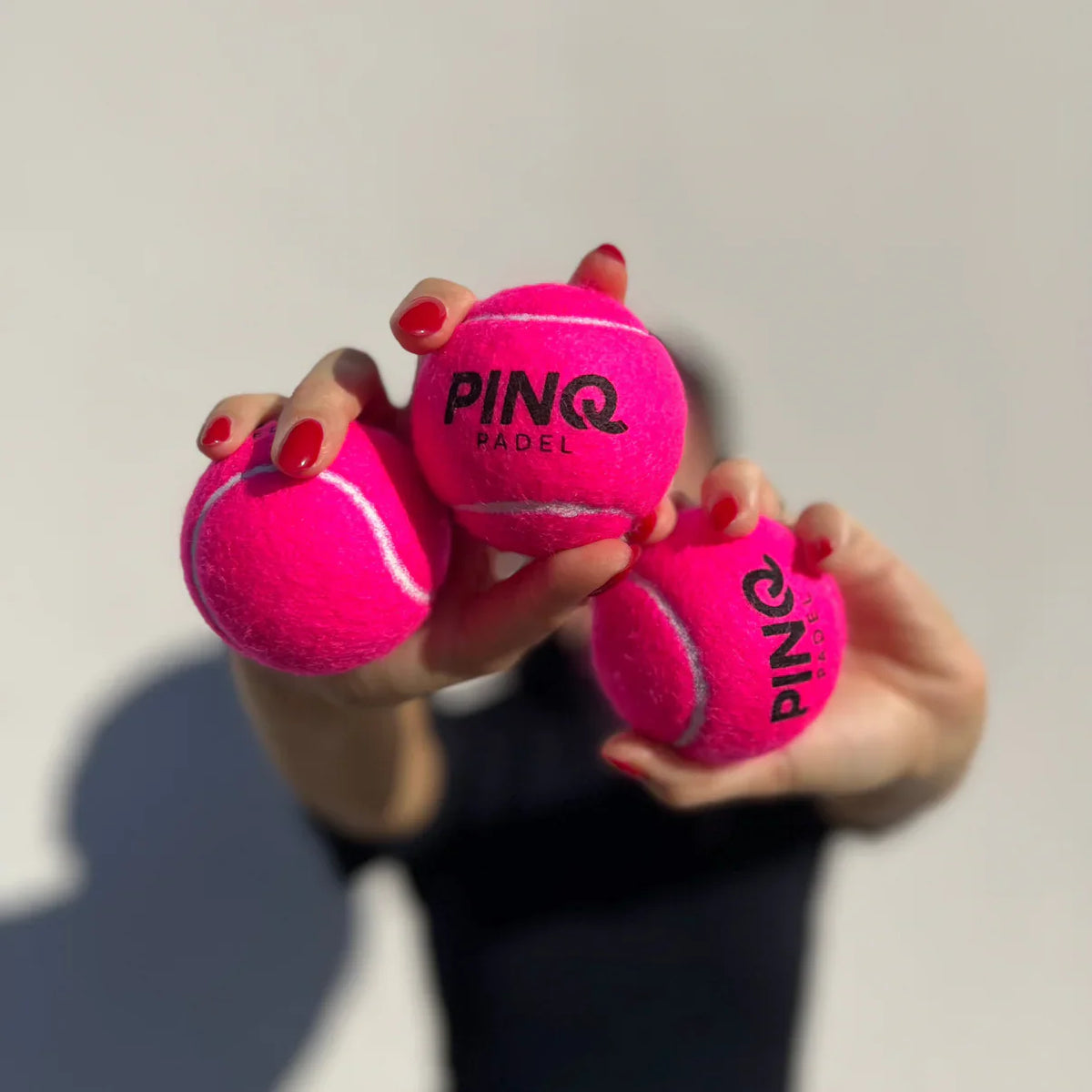Player holding three pink PINQ padel balls towards the camera